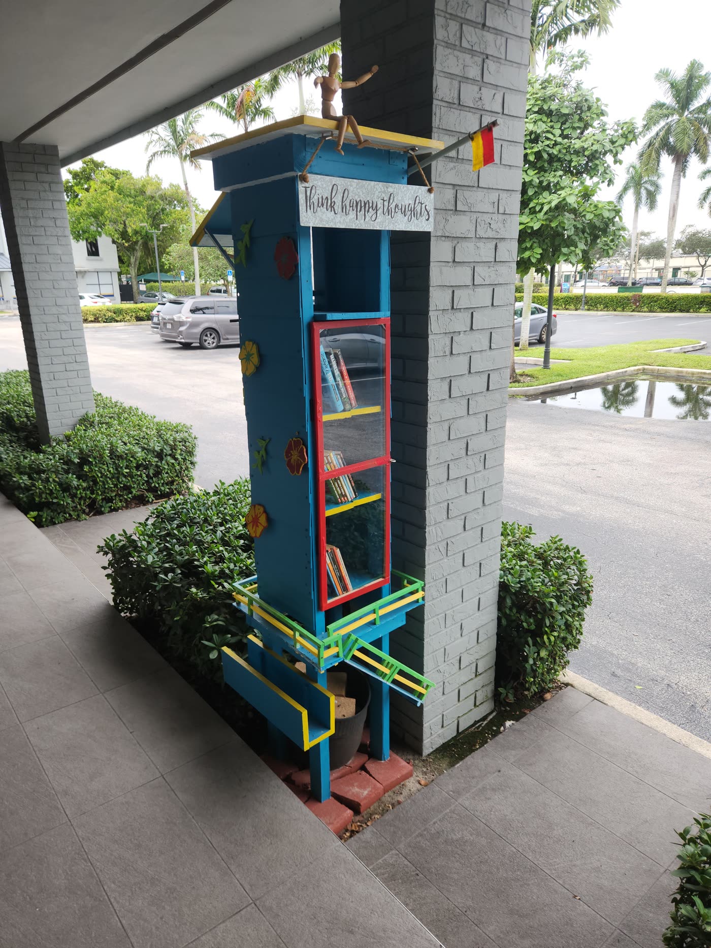 The free book exchange outside Swami Juice — a hand-built blue lifeguard tower with a red glass door full of books and a Think Happy Thoughts sign