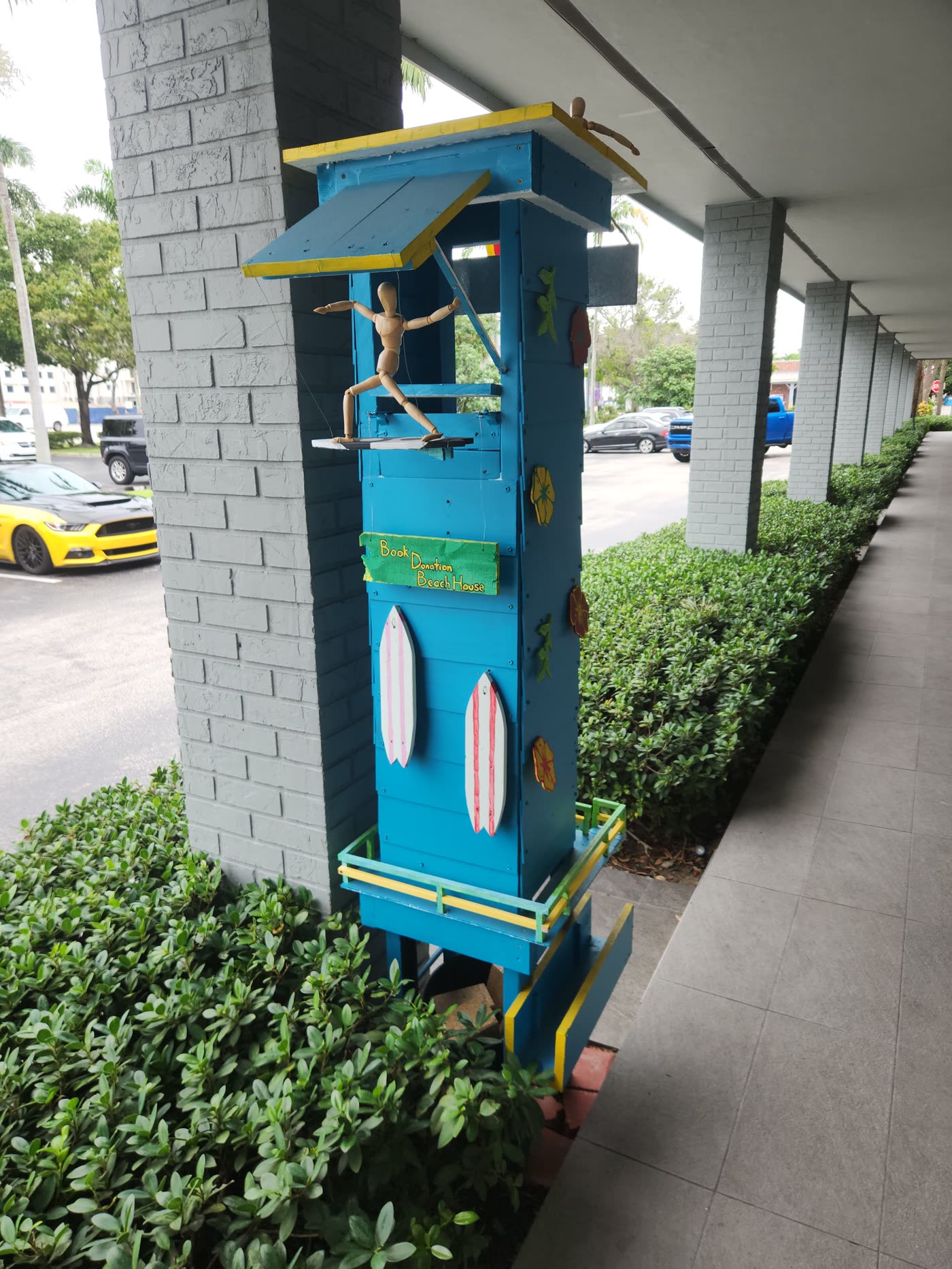 The free book exchange outside Swami Juice — a hand-built lifeguard tower painted blue, with a wooden artist mannequin surfing off the roof