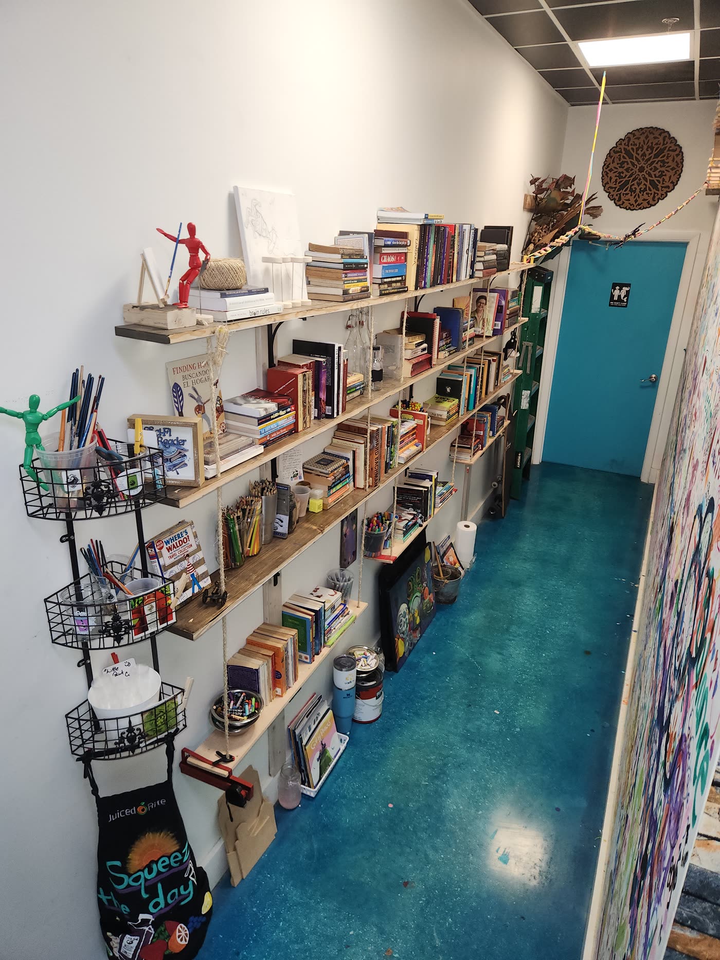 The reference shelves inside Swami Juice — books and jars of brushes and colored pencils sharing the same shelves