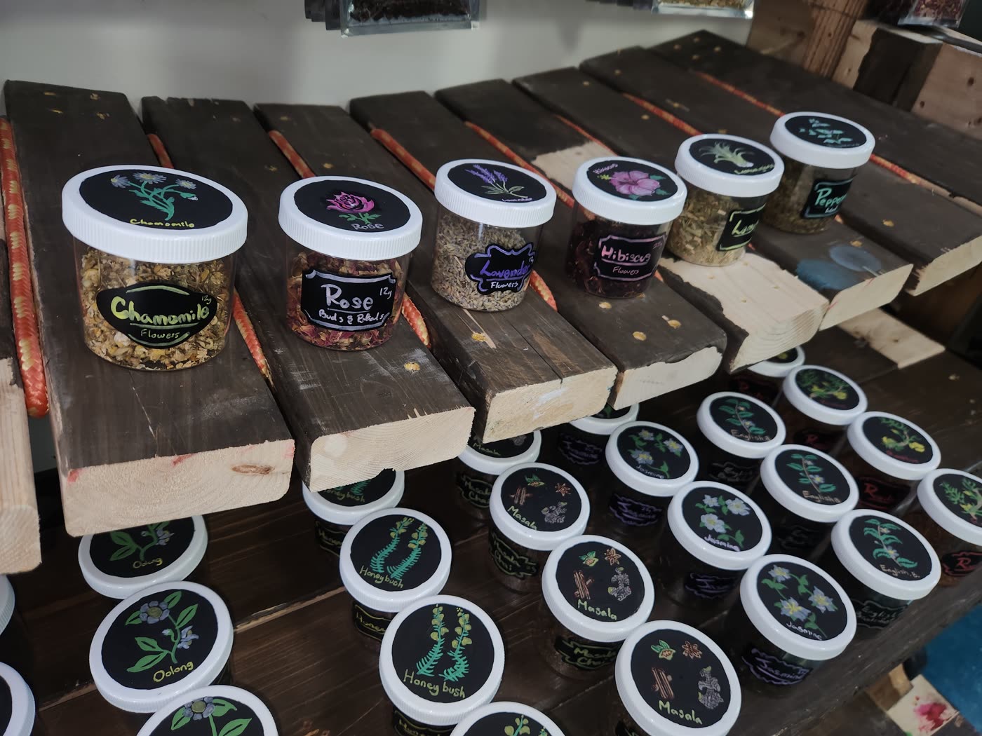 Hand-painted tea jars on a curved shelf at Swami Juice — each black lid painted with the botanical that is inside the jar