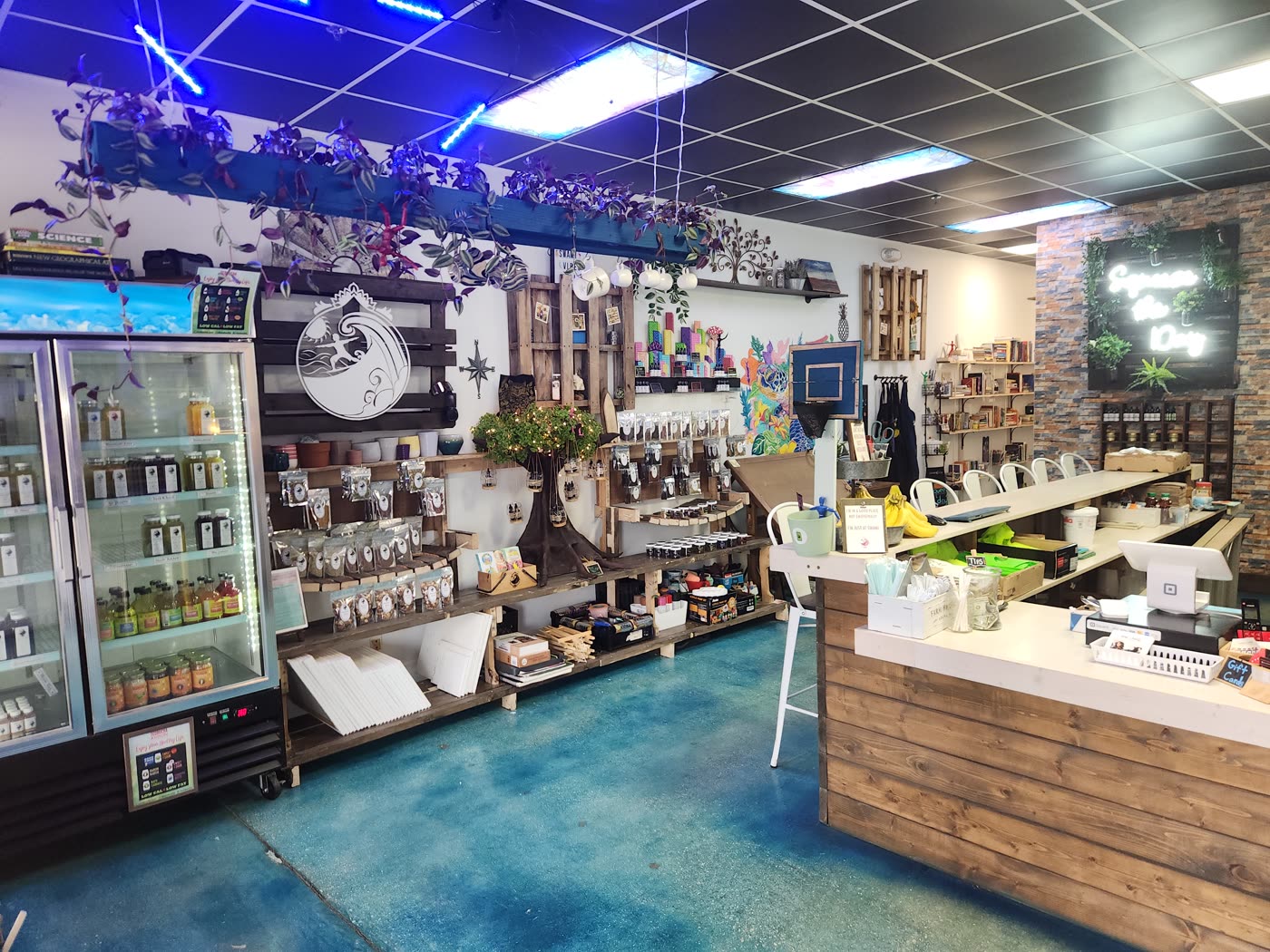 Inside Swami Juice — the retail wall, blue floor, and the Squeeze the Day neon over the bar