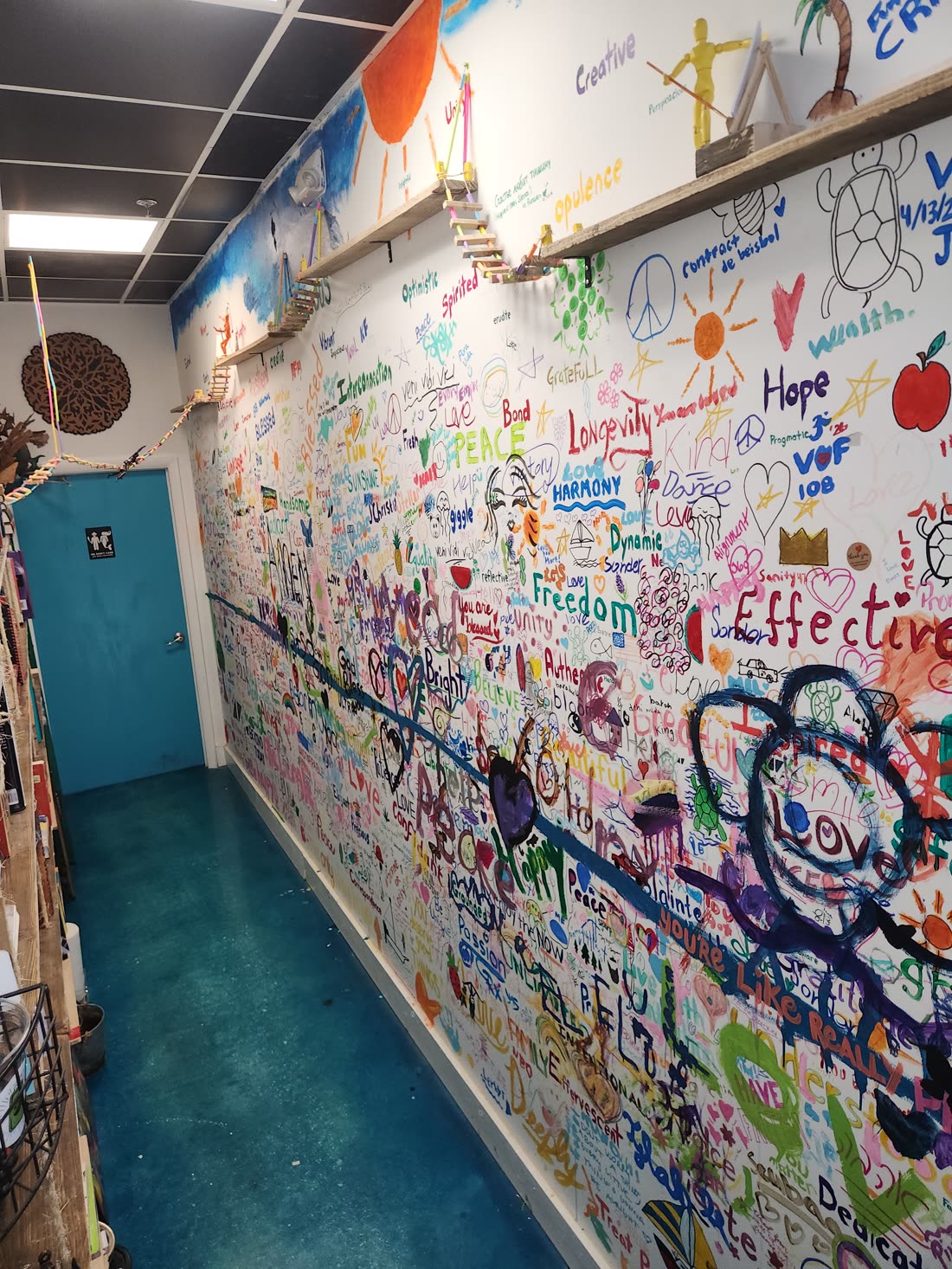 The Wishing Wall at Swami Juice — a hallway wall covered floor to ceiling in hand-painted words and drawings left by visitors